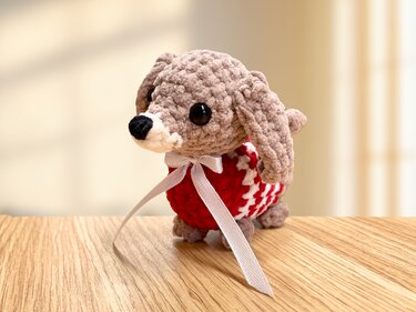 Handgehäkelter Amigurumi-Hund mit rot-weißem Pullover und weißer Schleife auf Holz