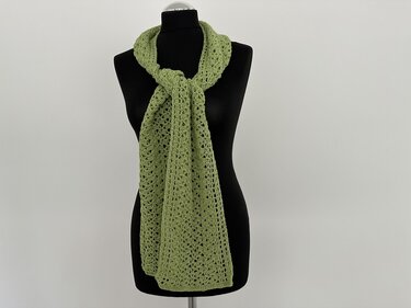 Lindgrüner gehäkelter Schal mit Lochmuster an einer schwarzen Schaufensterpuppe, vorne locker geknotet