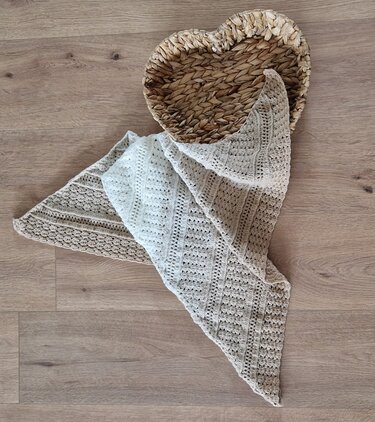 Gehäkeltes, zweifarbiges Dreieckstuch in Creme und Beige auf hellem Holzboden neben einem herzförmigen Korb.