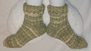 Paar gehäkelter Socken in grün-beige Melange auf weißen Fußformen