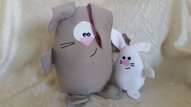 Zwei Stoffhasen, ein großer beigefarbener und ein kleiner weißer Hase mit runden Körpern, gestickten Gesichtern und applizierten Ohren, auf hellem Stoff