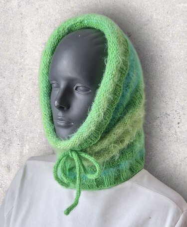 Flauschiger grüner Schlauchschal mit Kapuze und Bindeband auf Mannequin.