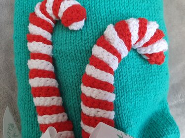 Zwei rot-weiß gestreifte gestrickte Zuckerstangen auf türkisfarbenem Strickstoff.