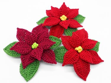 Detailansicht von drei gehäkelten Weihnachtssternen mit sichtbaren Maschen und grünen Blättern