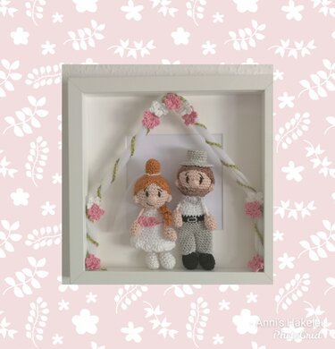 Gehäkelte Amigurumi-Braut und Bräutigam in weißem Rahmen mit Blumenbogen