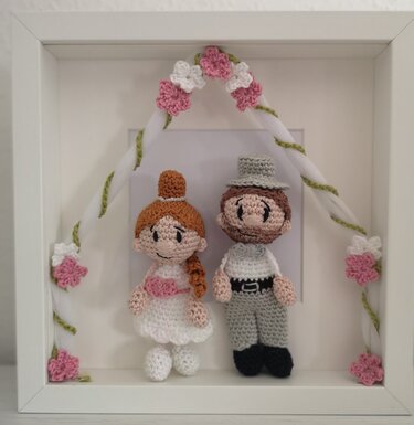 Gehäkelte Braut- und Bräutigam-Amigurumi im Bilderrahmen mit Häkelblumenbogen