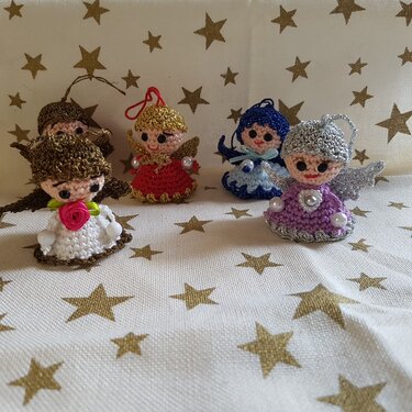 Fünf gehäkelte Engelchen-Amigurumi mit Flügeln und glitzernden Details auf einem Sternmuster-Tuch