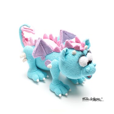 Gehäkelter Amigurumi-Drache in Hellblau mit rosa und lila Akzenten und großen Augen vor weißem Hintergrund
