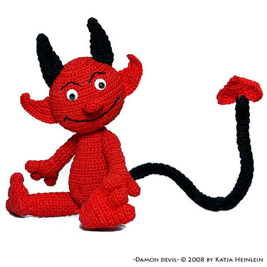 Red crochet amigurumi devil with black horns, curled tail, and stitched smile on white background