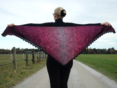 Geöffnete Ansicht eines gestrickten Dreieckstuchs mit Streifenmuster und Lochkante, gehalten von einer Person von hinten