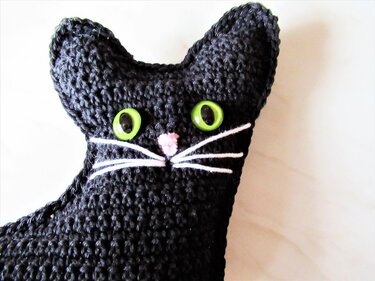 Schwarze gehäkelte Katze mit grünen Augen und rosa Nase