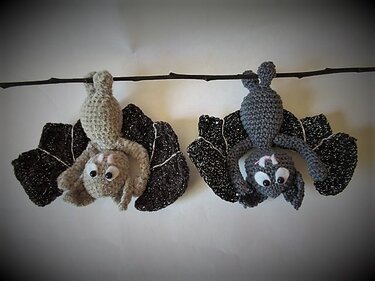 Zwei gehäkelte Fledermäuse (hellgrau und dunkelgrau) hängen kopfüber an einem Ast