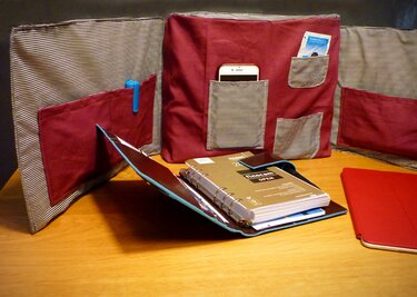 Drei bordeauxrote Stofforganizer mit gestreiften Taschen, bestückt mit Smartphone und Stift, neben einem Ringordner und Tablet auf Holz