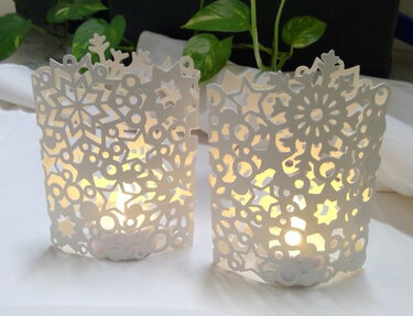 Zwei weiße Papierwindlichter mit filigranen Schneeflocken-, Stern- und Kreismustern, innen beleuchtet