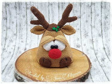 Handgehäkeltes Rentier-Amigurumi mit roter Nase, Geweih und Blattdekor auf Holzscheibe