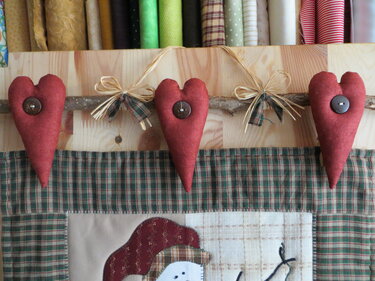 Drei längliche, rotbraune Stoffherzen mit Knöpfen an einem Ast