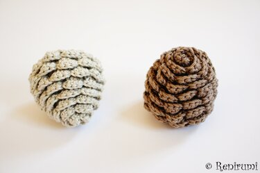 Zwei gehäkelte Tannenzapfen, einer beige, einer braun, mit schuppenartigem Muster auf hellem Hintergrund