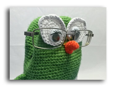 Grüne gehäkelte Amigurumi-Eule mit weißen Augen, aufgesetzter Brille und orangefarbenem Schnabel vor weißem Hintergrund.