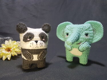 Gehäkelte Amigurumi-Figuren: schwarz-weißer Panda neben mintgrünem Elefanten auf dunklem Hintergrund
