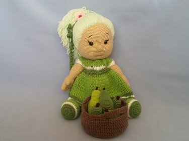 Crocheted amigurumi doll in a green dress with a brown basket of crocheted pears.