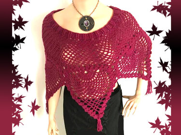 Beerenfarbener gehäkelter Poncho mit durchbrochenem Ajourmuster und Quasten auf einer Schaufensterpuppe.