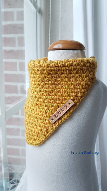 Mustard yellow crocheted baby cowl with a small tag reading 'baby' on a mannequin torso.