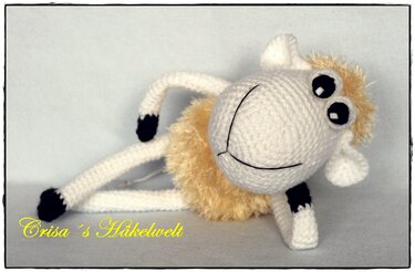 Liegendes gehäkeltes Amigurumi‑Schaf mit flauschigem gelb‑beigem Körper und schwarzen Hufen