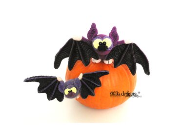 Zwei gehäkelte lila-schwarze Amigurumi-Fledermäuse mit gelben Augen auf einem orangefarbenen Kürbis