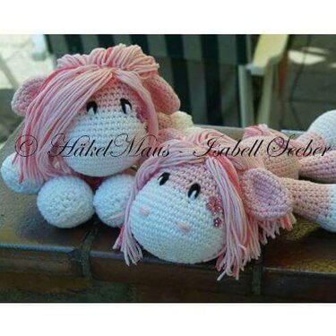Zwei gehäkelte Amigurumi in Rosa und Weiß mit langen Garn-Mähnen und gestickten Augen