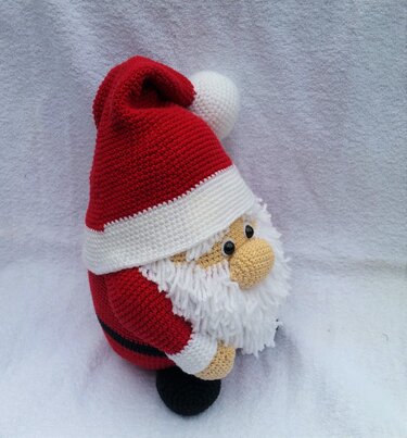 Gehäkelter Weihnachtsmann-Amigurumi mit roter Mütze, weißem Bommel, weißem Bart und schwarzem Gürtel auf hellem Stoff