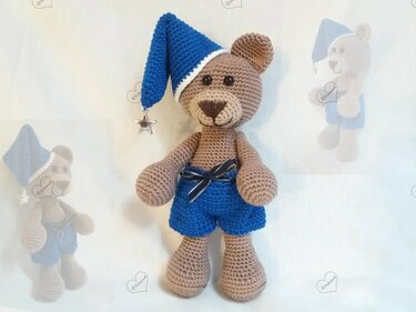 Brauner gehäkelter Teddybär mit blauer Zipfelmütze, Sternanhänger und blauen Shorts.