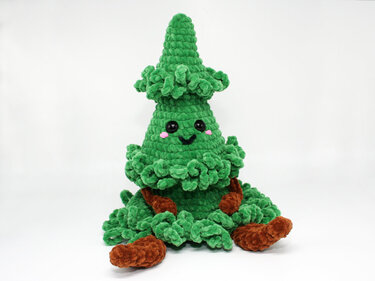 Green ruffled crochet amigurumi Christmas tree with black eyes, pink cheeks and brown legs on white background