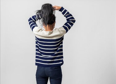 Person von hinten in gestreiftem Strickpullover und Jeans, Haare hochgebunden