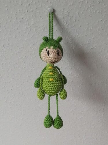 Grüner gehäkelter Amigurumi-Schlüsselanhänger mit Fühlern und langen Beinen, an Wandhaken hängend