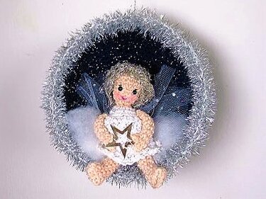 Gehäkeltes Amigurumi-Engelchen mit Tüllflügeln in runder Weihnachtskugel mit silbernem Rand