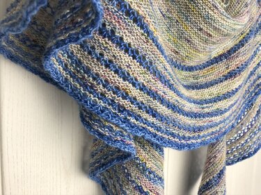 Nahaufnahme der Maschenstruktur eines halbrunden Stricktuchs in Pastellfarben mit blauer Kante und Lochreihen