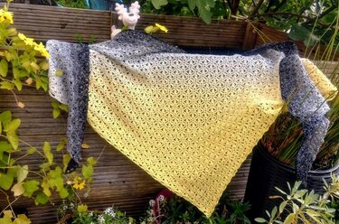 Grey-to-yellow triangle crochet shawl with lacy openwork draped on a wooden fence