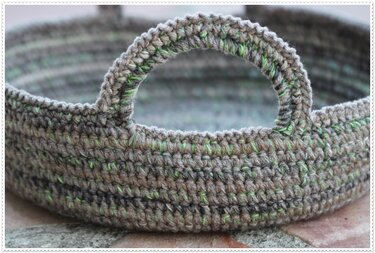 Round crocheted basket with two handles, variegated grey-brown yarn with green flecks.