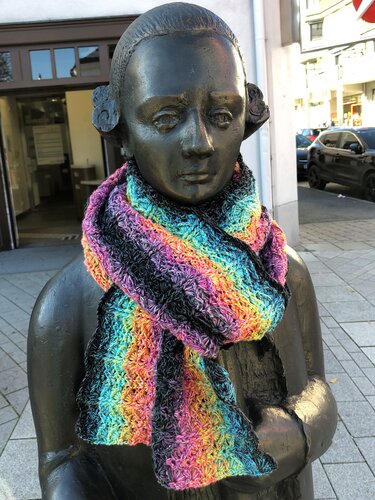 Mehrfarbiger gehäkelter Loop mit Farbverlauf und dunklen Streifen an einer Bronze-Statue