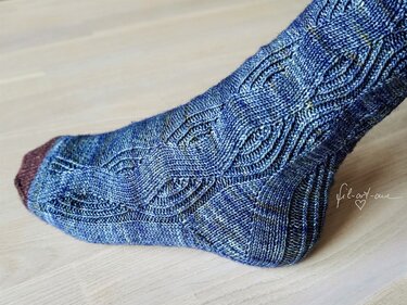 Blue variegated knitted sock with lace-cable pattern and contrasting brown toe