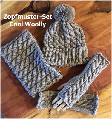 Graues Zopfmuster-Strickset mit Bommelmütze, Loop-Schal und fingerlosen Stulpen auf Holz.
