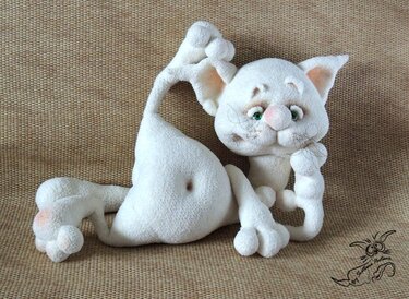 weiße gehäkelte Amigurumi-Katze mit gebogenem Schwanz und grünen Augen, liegend