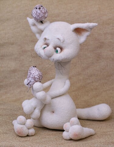 Cremefarbene gehäkelte Amigurumi-Katze sitzt und hält zwei gemusterte Stoffvögel