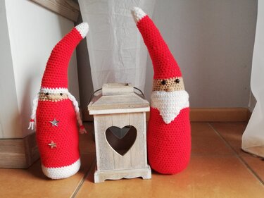 Zwei gehäkelte Weihnachtswichtel in Rot und Weiß neben einer Holzlaterne