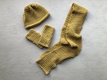 Gehäkeltes Set aus Mütze, zwei Handstulpen und langem Schal in Senfgelb auf hellgrauem Untergrund