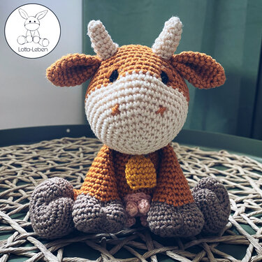 Seated crochet amigurumi cow in brown and cream with yellow bell