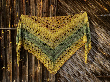 Triangle crochet shawl in yellow-to-green gradient with lace bands and scalloped edge hung flat on wooden doors