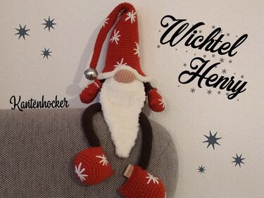Gehäkelter roter Wichtel mit langer Mütze und weißem Bart sitzt auf Sofalehne