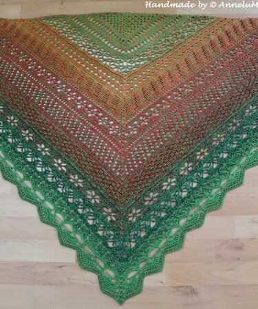 Crochet triangle shawl in green, orange and red gradient with floral openwork and scalloped edge.