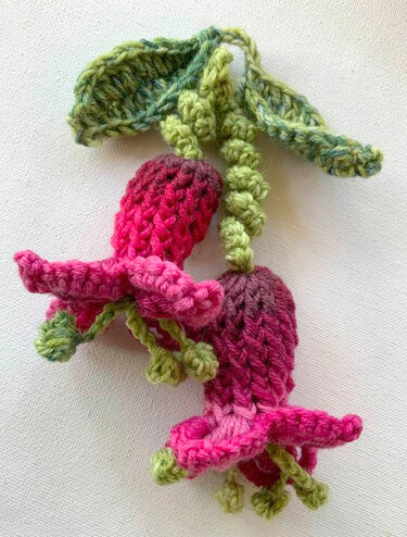 Zwei gehäkelte Fuchsienblüten in Pink-Violett mit grünen Blättern